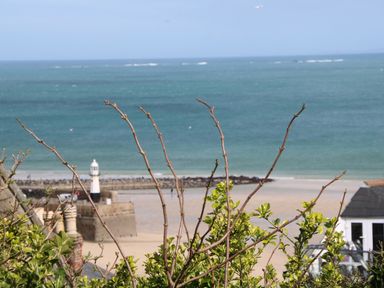 A beach view with a lighthouse and sea with some plants and a building in the foreground at Little Valley View in Angarrack