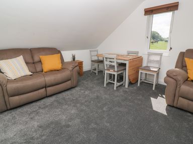 A sitting room with two brown sofas a wooden dining table with four chairs and a window showing a grassy field at Little Valley View in Angarrack