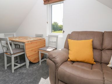 A room with a brown sofa with a yellow cushion a wooden dining table with four chairs and a window showing grass and trees at Little Valley View in Angarrack