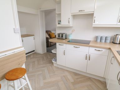 A kitchen with white cabinets wooden countertops a toaster kettle three labeled canisters and a bar stool at Little Valley View in Angarrack
