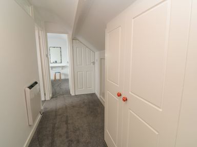 A hallway with carpeted floor cupboards and a door leading to a room with a stool and mirror at Little Valley View in Angarrack