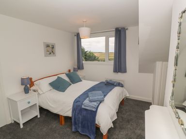 A bedroom with a bed blue cushions and throws bedside tables and lamps a window with curtains and a mirror at Little Valley View in Angarrack