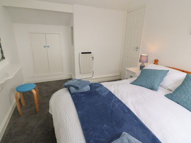 A bedroom with a bed with blue cushions and blanket a bedside table with lamp a small blue stool and a white door at Little Valley View in Angarrack