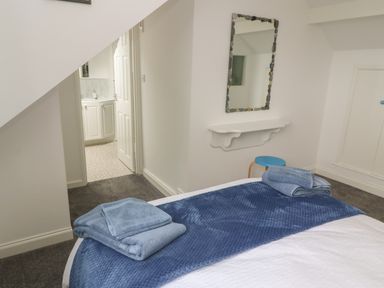 A bedroom with a bed covered with blue blankets towels on the bed a mirror a shelf and a stool at Little Valley View in Angarrack