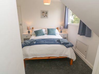 A bedroom with a double bed blue pillows and blankets bedside tables with lamps and a window with curtains at Little Valley View in Angarrack
