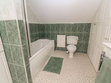 A bathroom with a bathtub toilet green tiles and storage cabinets at Little Valley View in Angarrack