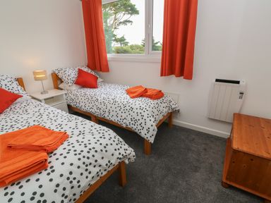 A bedroom with two single beds with polka dot bedding and orange pillows and curtains at Little Valley View in Angarrack