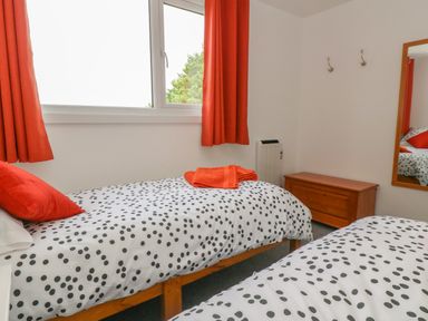 A bedroom with two single beds with polka dot bedding orange curtains and a wooden chest at Little Valley View in Angarrack