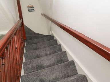 A carpeted staircase with wooden handrails on both sides and a wall decoration at Little Valley View in Angarrack