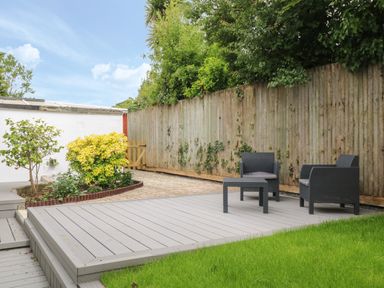 A garden area with gray deck chairs and a table on a wooden platform next to a grassy lawn at Little Valley View in Angarrack