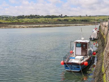 A small boat named Lady Wendy moored alongside a stone wall in a calm body of water with a green landscape and a church in the distance at Little Valley View in Angarrack
