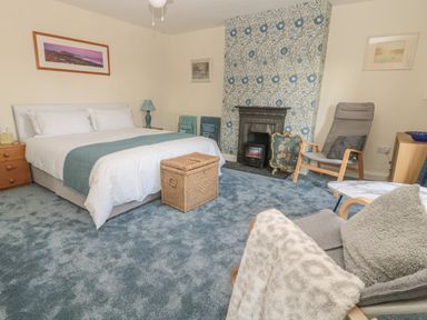 A bedroom with a bed bedside tables a fireplace two chairs and blue carpet at Wordsworth Cottage West in Longframlington