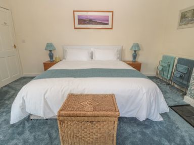A bedroom with a double bed two side tables with lamps a wicker basket and towel racks at Wordsworth Cottage West in Longframlington