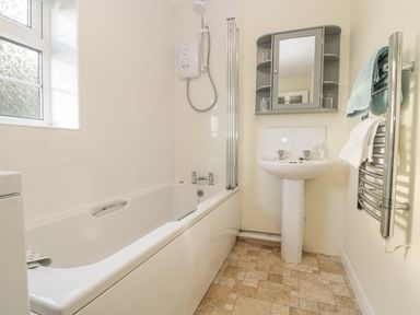 A bathroom with a bathtub shower unit pedestal sink mirrored cabinet and towel rail at Wordsworth Cottage West in Longframlington