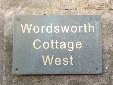 A metal sign with the text Wordsworth Cottage West mounted on a stone wall at Wordsworth Cottage West Longframlington
