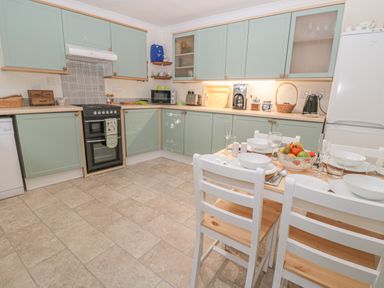 A kitchen with green cabinets a black oven a dining table with white chairs and a fruit bowl at Wordsworth Cottage West in Longframlington