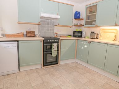 A kitchen with green cabinets a black oven a dishwasher a microwave and a toaster at Wordsworth Cottage West in Longframlington