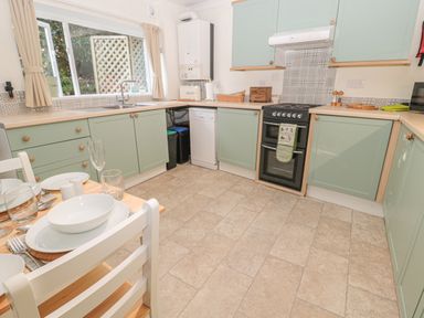 A kitchen with pale green cabinets a dining table set with dishes and glasses at Wordsworth Cottage West in Longframlington
