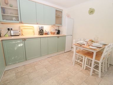 A kitchen with green cabinets a refrigerator a wooden dining table set with dishes and glasses and a wall clock at Wordsworth Cottage West in Longframlington