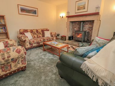 A living room with patterned sofas a green armchair a wooden coffee table and a fireplace at Wordsworth Cottage West in Longframlington