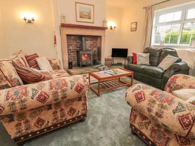 A living room with patterned sofas a leather sofa a wood burning stove and a coffee table at Wordsworth Cottage West in Longframlington