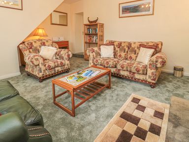 A living room with patterned armchairs and a sofa a wooden coffee table and a bookshelf at Wordsworth Cottage West in Longframlington
