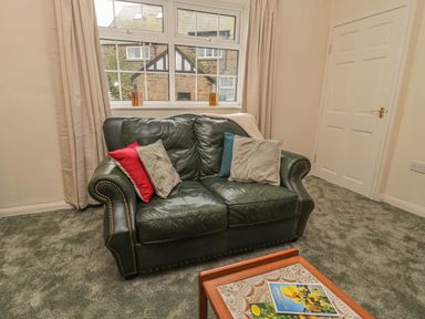 A sitting room with a green leather sofa cushions and a coffee table with magazines at Wordsworth Cottage West in Longframlington