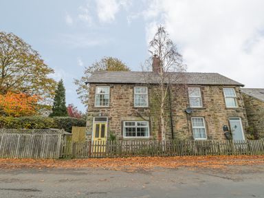 A stone cottage with yellow and blue doors and a wooden fence in front at Wordsworth Cottage West in Longframlington