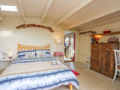 A bedroom with a wooden bed blue and white bedding a wooden dresser and a chair at Songbird Hideaway in Pwllheli