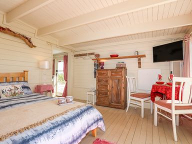 A bedroom with a wooden bed a small dining table with two chairs a wooden chest of drawers and a wall mounted television at Songbird Hideaway in Pwllheli