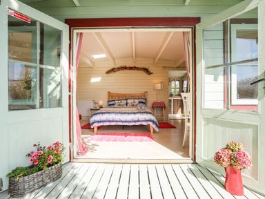 A bedroom with a bed a lamp and flowers on the floor at Songbird Hideaway in Pwllheli