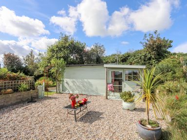 A small garden shed with a gravel patio and potted plants at Songbird Hideaway in Pwllheli