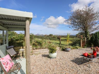 A gravel patio with potted plants and outdoor seating overlooking fields at Songbird Hideaway in Pwllheli