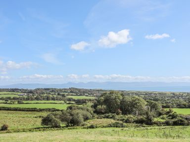 A landscape view of green fields trees and hills under a blue sky at Songbird Hideaway in Pwllheli