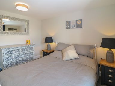 A bedroom with a bed with gray bedding two bedside tables with lamps a patterned dresser and a large mirror on the wall at Rosebank Cottage in Mortehoe