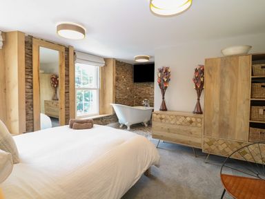 A bedroom with a bed a freestanding bathtub wooden furniture and a large window at Rosebank Cottage in Mortehoe