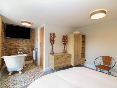 A bedroom with a freestanding bathtub near a stone wall a wooden dresser a wooden wardrobe and a chair at Rosebank Cottage in Mortehoe