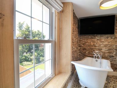 A bathroom with a freestanding bathtub and a mounted television on a stone wall at Rosebank Cottage in Mortehoe