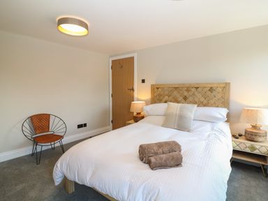 A bedroom with a double bed a wooden headboard two bedside tables with lamps a chair and folded towels on the bed at Rosebank Cottage in Mortehoe