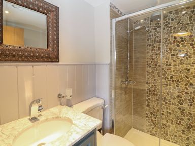 A bathroom with a sink and faucet a toilet and a shower with pebble tile walls at Rosebank Cottage in Mortehoe