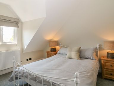 A bedroom with a white metal bed frame grey bedding a beige pillow two wooden nightstands with lamps a window and a radiator at Rosebank Cottage in Mortehoe