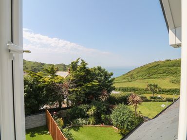 A view of a garden with trees and hills in the background taken from a window at Rosebank Cottage in Mortehoe