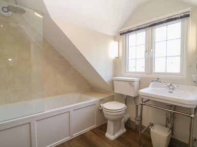 A bathroom with a bathtub under a slanted ceiling next to a toilet and a sink under a window at Rosebank Cottage in Mortehoe
