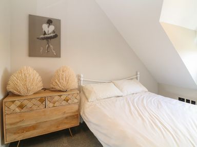 A bedroom with a bed next to a wooden dresser with two lamps and a ballerina painting on the wall at Rosebank Cottage in Mortehoe