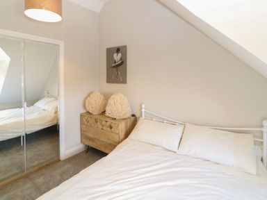 A bedroom with a bed, wooden chest of drawers, decorative items, and a mirrored wardrobe at Rosebank Cottage in Mortehoe