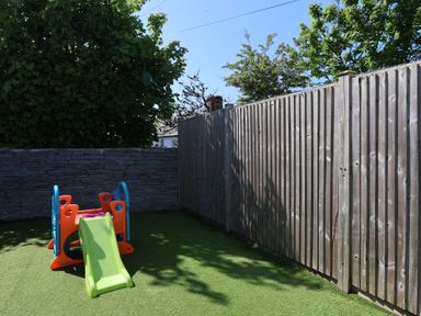 A small playground with a plastic slide on artificial grass surrounded by wooden and stone fences at Rosebank Cottage in Mortehoe