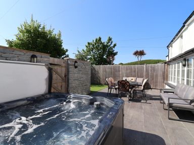 An outdoor patio with a hot tub a dining table with chairs and a cushioned sofa at Rosebank Cottage in Mortehoe