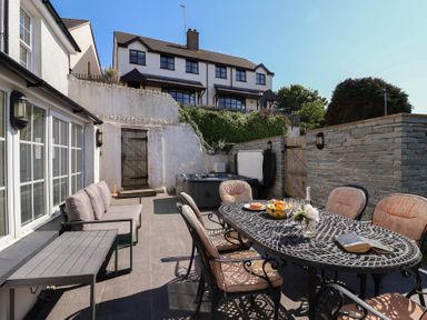 An outdoor patio area with a dining table and chairs a sofa a coffee table and a hot tub at Rosebank Cottage in Mortehoe