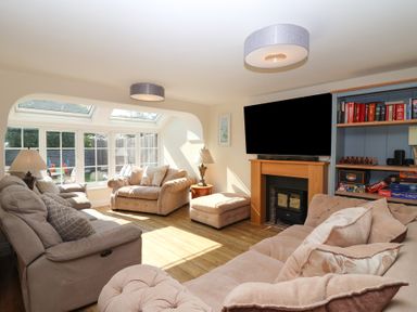 A living room with beige sofas wooden floor a fireplace with a TV above it and a bookshelf at Rosebank Cottage in Mortehoe