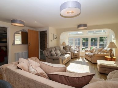 A living room with beige sofas pillows wooden floor and large windows at Rosebank Cottage in Mortehoe